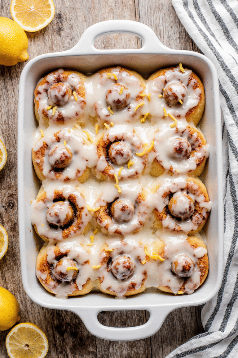 Freshly baked lemon sweet rolls topped with tangy lemon glaze in a white baking dish.