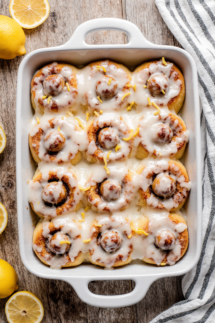 Freshly baked lemon sweet rolls topped with tangy lemon glaze in a white baking dish.